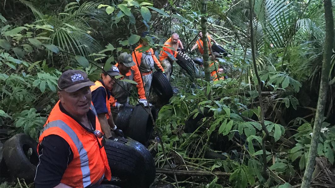 Many people in high visibility clothing remove old tires from a ravine.