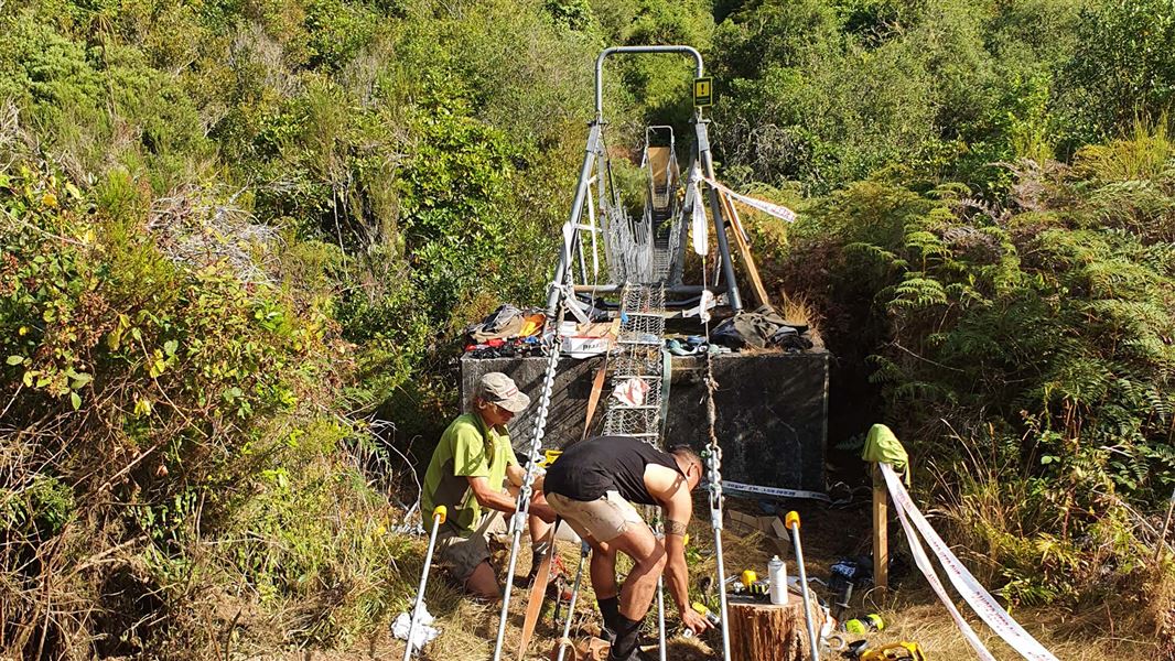 Two people fix one end of a metal swing bridge.