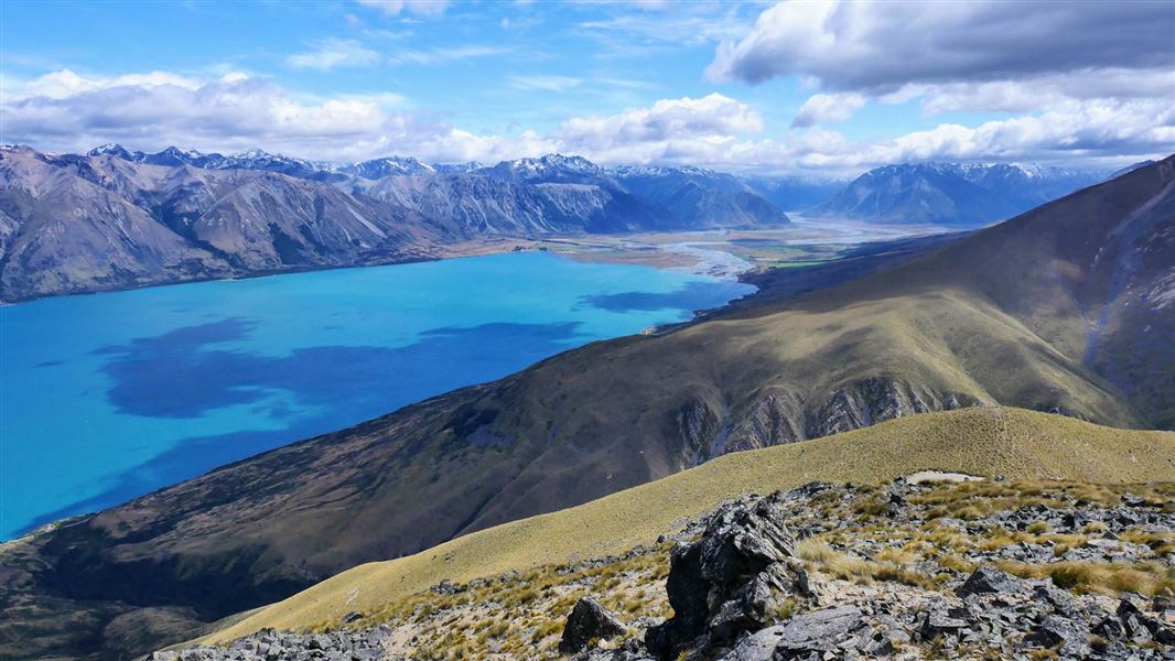 View from mountain top over turquoise lake  with a mountain range in the background. 