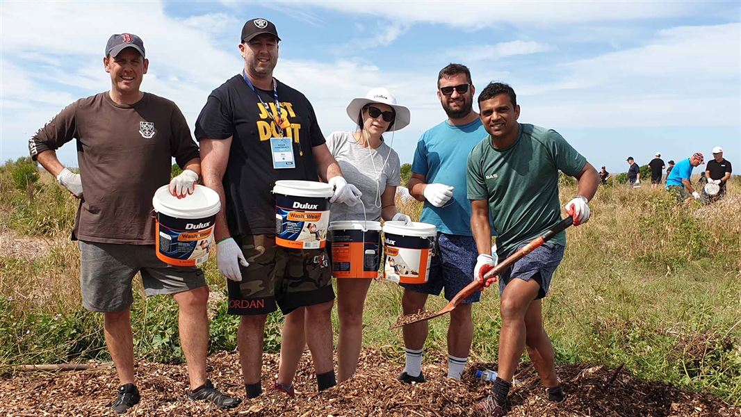 Four people helping plant trees. They're also holding Dulux paint buckets.