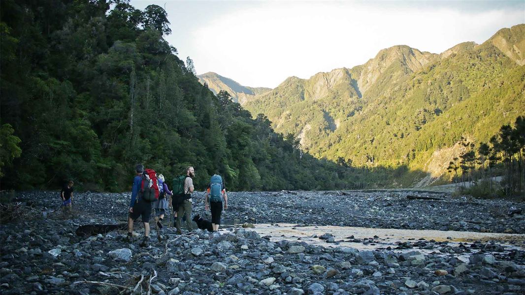 A group of trampers journey through a dried out river at the bottom of a valley.