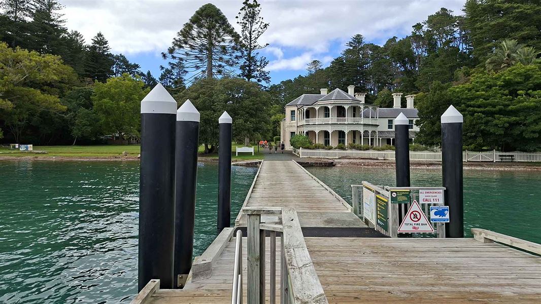 View from a dock of a large historic house and gardens beside the shore.