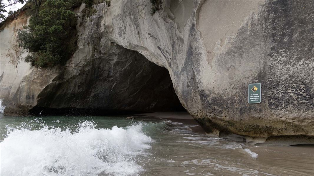 Surf rushing into an archway hewn in the side of a cliff.