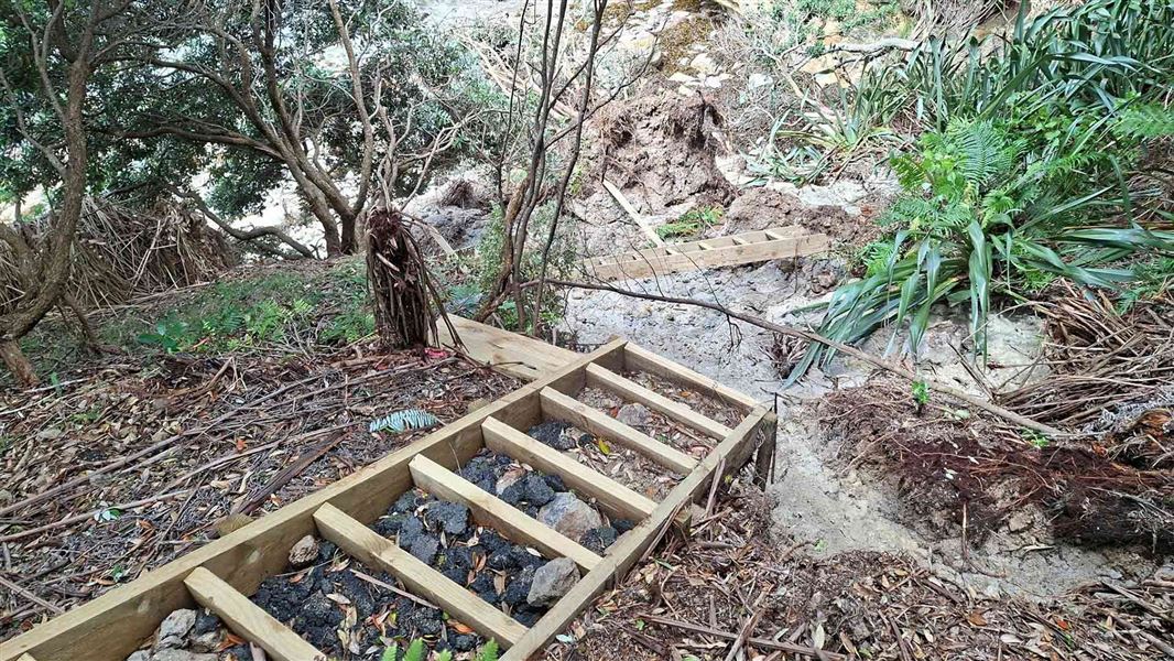 A set of wooden stairs with rocks and sand between its wooden frames and below it a broken section of stairs laying prone a few metres away.