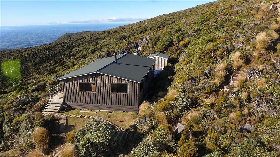 A large wooden hut perched on the side of a large hill overgrown with nature.