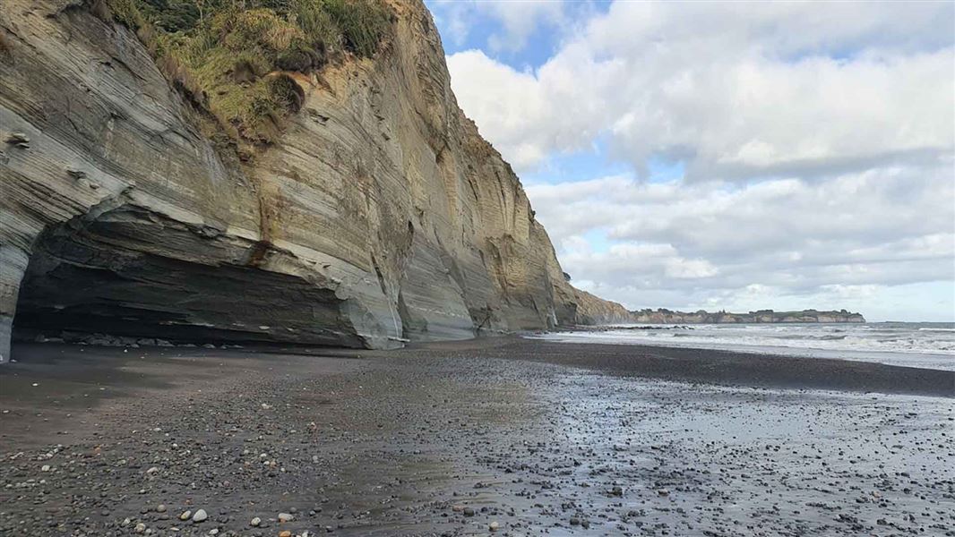 A large cliff stands tall next to a beach that looks out to sea.