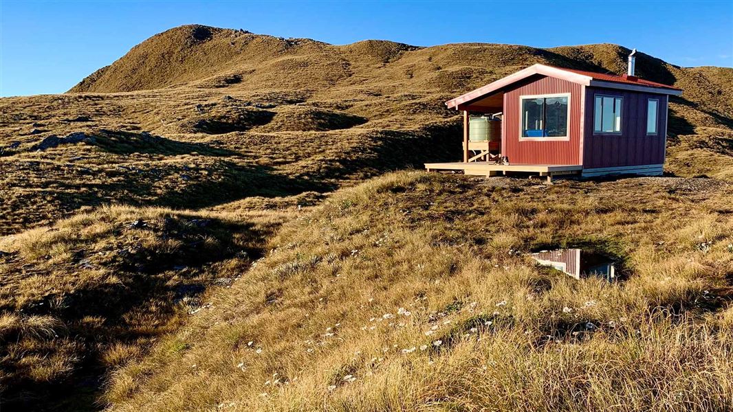 A small hut is perched on a small hill jutting out amongst long grassy hills.